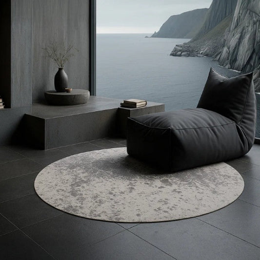 Modern interior with a round rug, gray cushions, and a view of water and mountains.