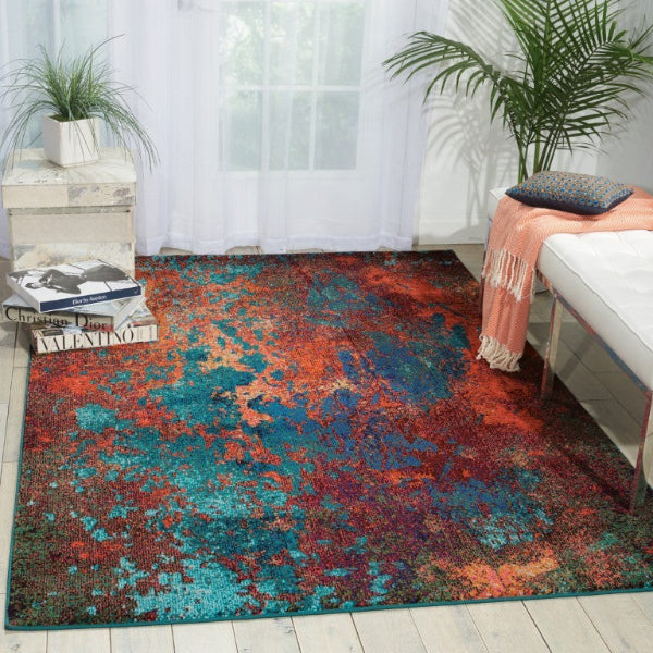 Multicolored area rug in a living room with books, a plant, and a sofa.
