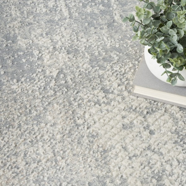 Close-up of a textured gray carpet with a plant and book in the corner.