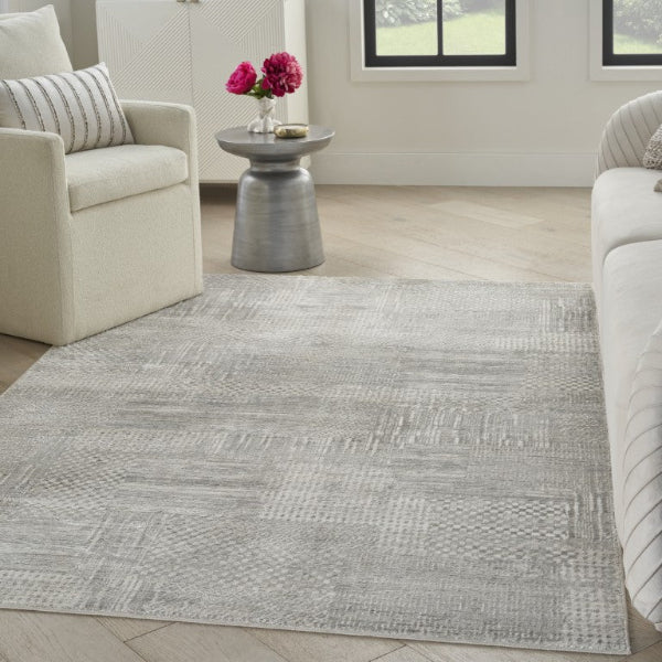Living room with a gray patterned rug, white armchair, and side table with flowers.