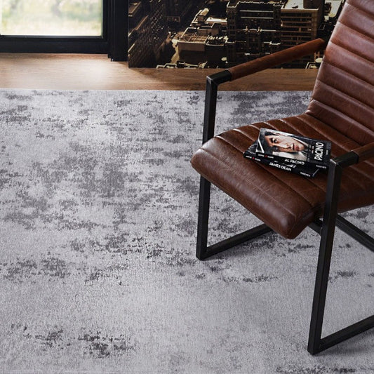 Brown chair with a magazine on a textured gray rug in a room with large windows.