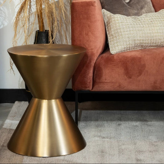 Gold side table in front of a pink sofa with decorative pillows.