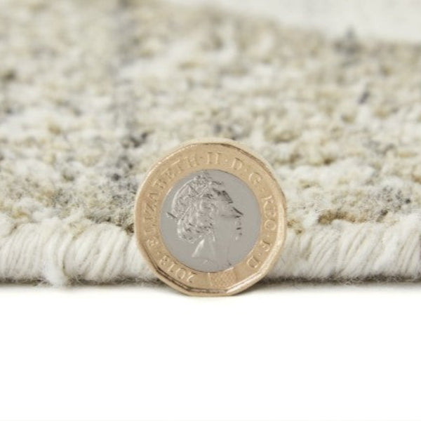Close-up of Concept Looms Dune Rug edge showing texture and thickness with a British pound coin for scale