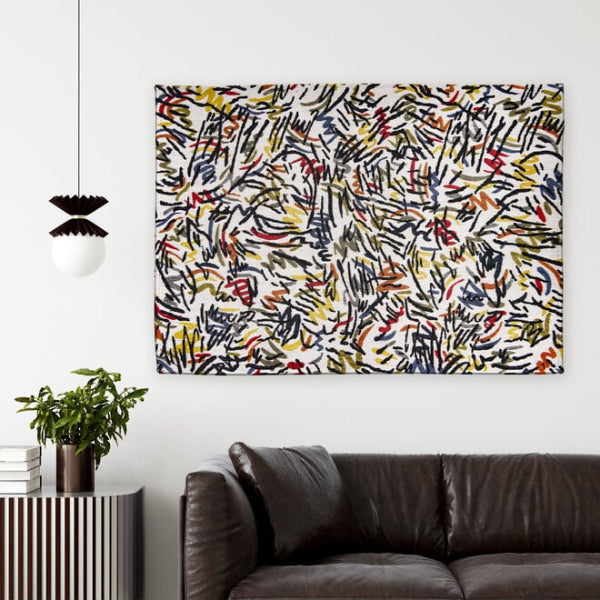 Louis De Poortere Dora and Graffito rug with abstract multicolour pattern displayed on a white wall above a dark brown leather sofa