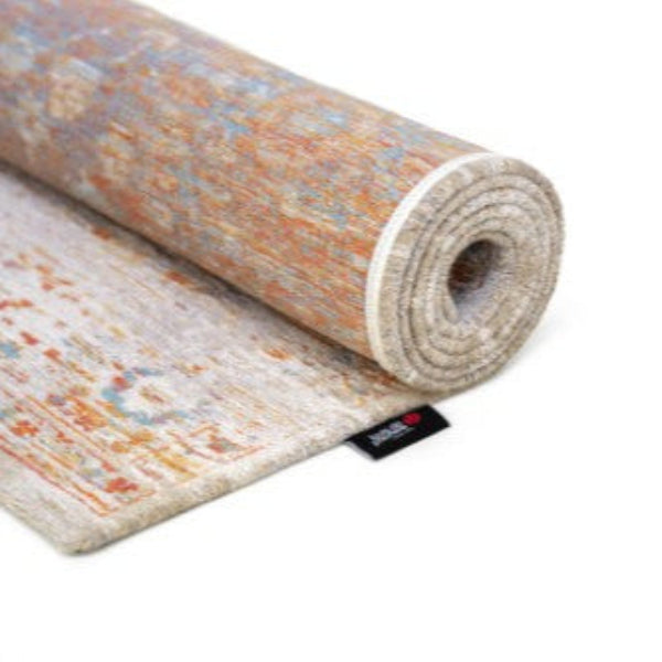 Rolled Louis De Poortere Ushak rug showing intricate vintage floral patterns in muted blue and orange tones