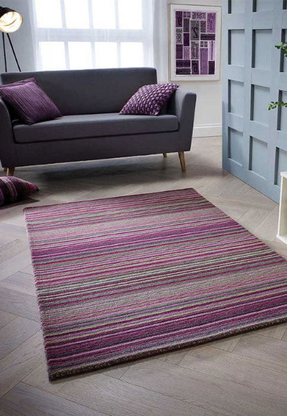 Melrose Carter stripes rug in purple and grey tones placed in a modern living room with a dark grey sofa