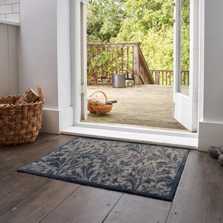 Turtle Mats Thistle Design indoor Mat with blue and grey floral pattern placed by an open door on wooden floor