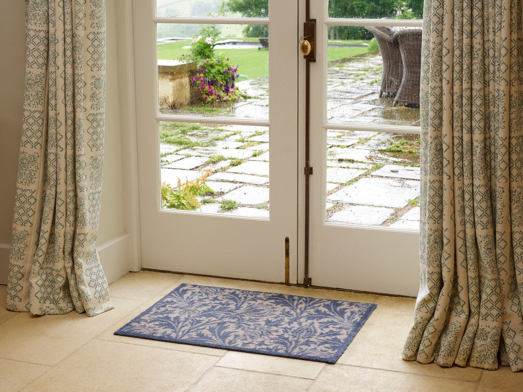 Turtle Mats Thistle Design indoor Mat in blue placed by glass French doors with patterned curtains