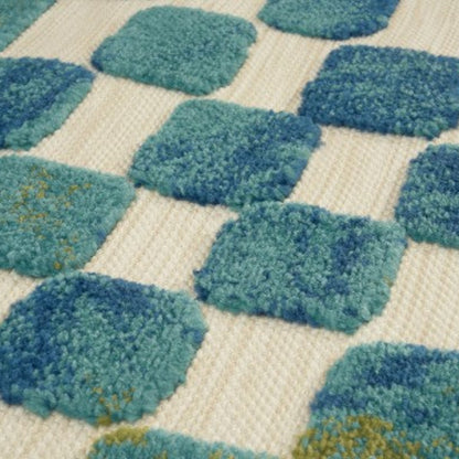 Close-up of a textured rug with blue and green diamond patterns on a beige background