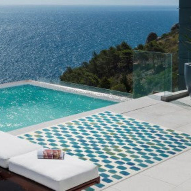 Pool area with lounge chairs and a colorful rug overlooking the ocean.