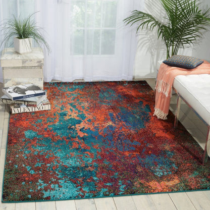 Multicolored area rug in a living room with books, a plant, and a sofa.