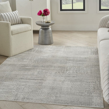 Living room with a gray patterned rug, white armchair, and side table with flowers.