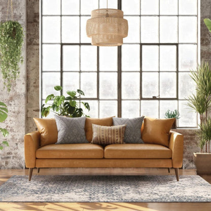 Brown sofa in a room with large windows, plants, and a rug.