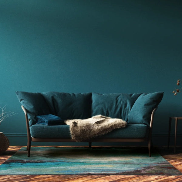 Teal sofa in a room with a dark teal wall and wooden floor.