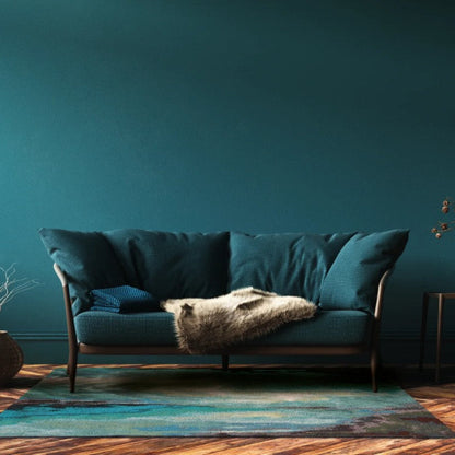 Teal sofa in a room with a dark teal wall and wooden floor.