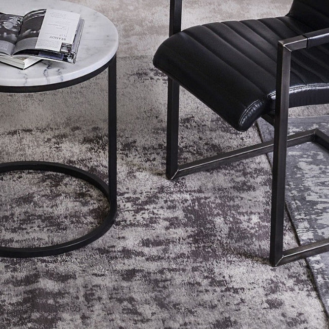Black chair and round side table on a textured gray rug