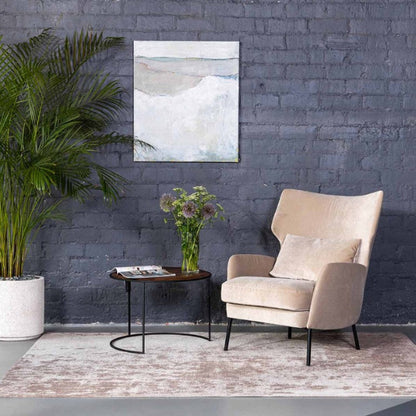 Beige armchair in a room with a gray brick wall, a plant, and a small table with a vase.