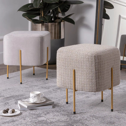 Two upholstered stools with gold legs in a room with a plant and small table.
