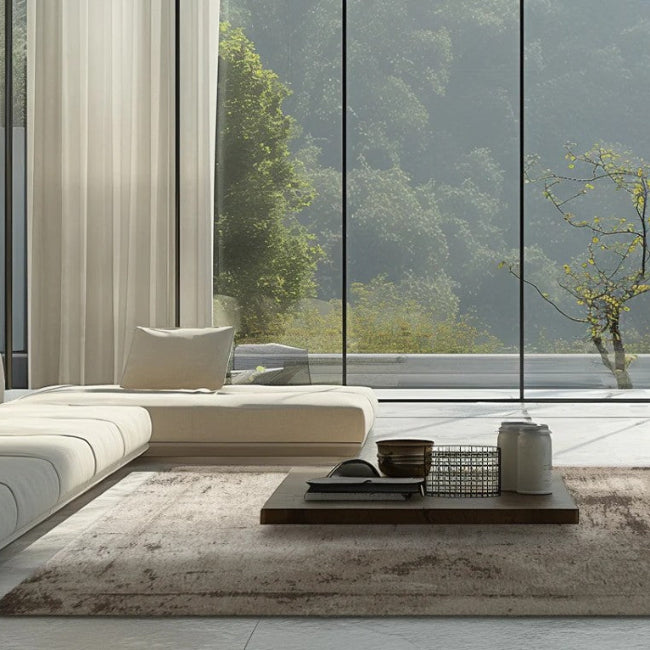 Modern living room with a sectional sofa, coffee table, and large windows overlooking trees.