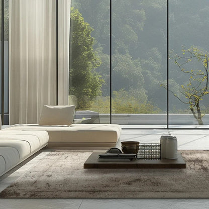 Modern living room with a sectional sofa, coffee table, and large windows overlooking trees.