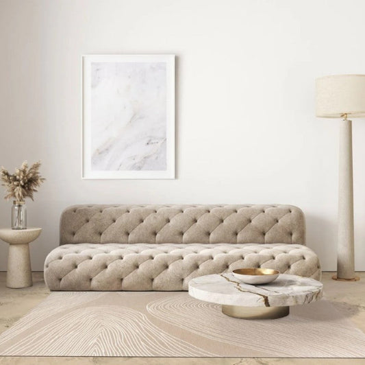 Beige tufted sofa in a modern living room with a marble coffee table and abstract art.