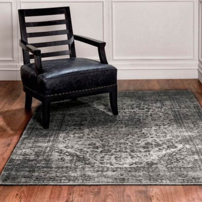 Black chair on a grey area rug in a room with wooden flooring and white walls.