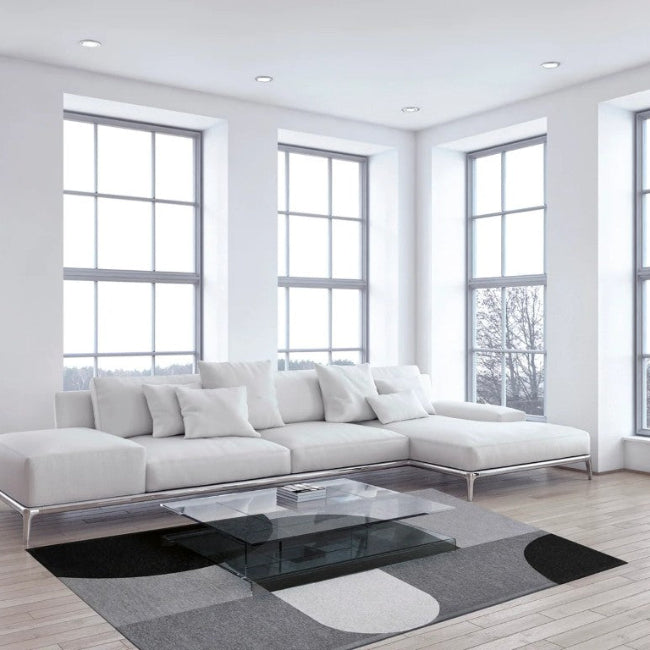 Modern living room with a white sofa, glass coffee table, and large windows.