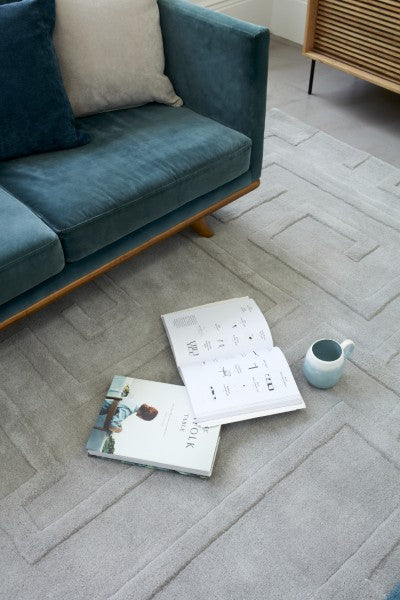 Luxury Asiatic Contemporary Plains Collection Maze Rug in soft grey under a blue sofa with books and a mug