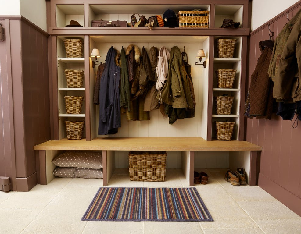 Turtle Mat in striped design placed in a rustic entryway with coats and baskets