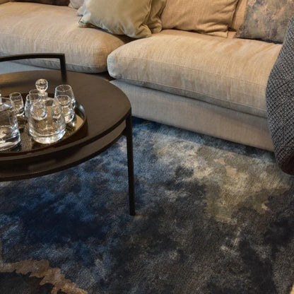 Round coffee table with glassware in front of a beige sofa on a textured blue rug.