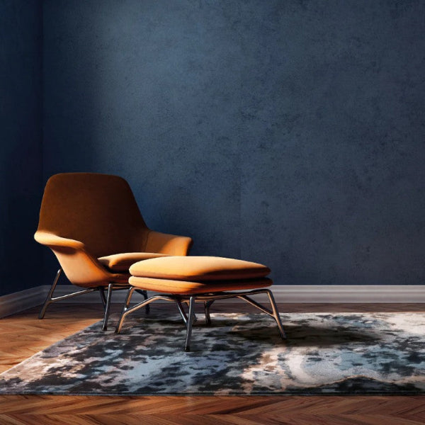 Orange chair and ottoman on a patterned rug against a dark blue wall.