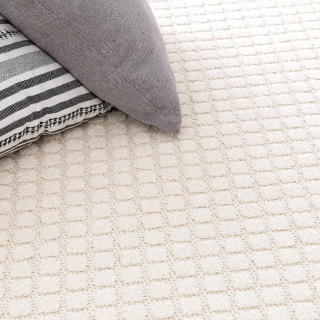 Textured white rug with a gray pillow and striped pillow on top