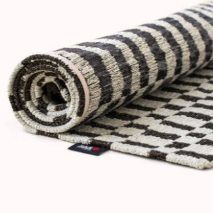 Rolled Louis De Poortere Berber Rug featuring black and white geometric patterns on luxury woven fabric