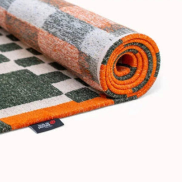 Rolled Louis De Poortere Chess rug featuring a modern geometric pattern with orange and green highlights