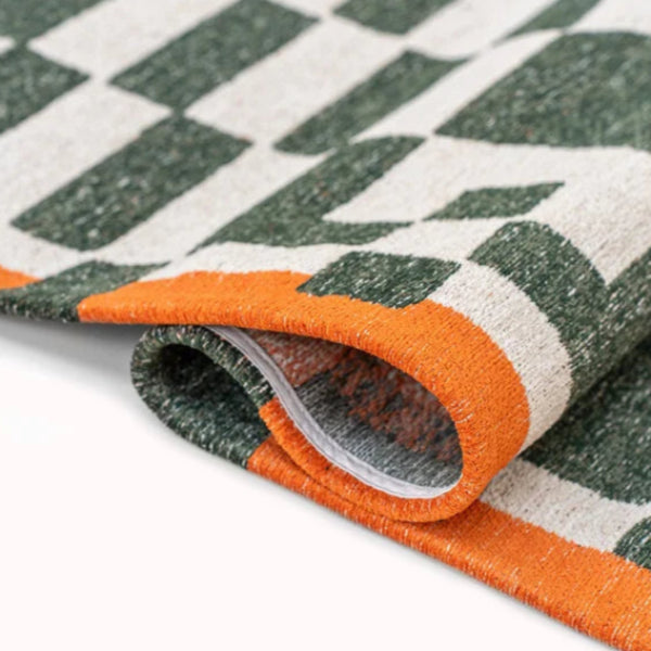 Close-up of folded luxury Louis De Poortere Chess rug featuring a green and white checkerboard pattern with orange border
