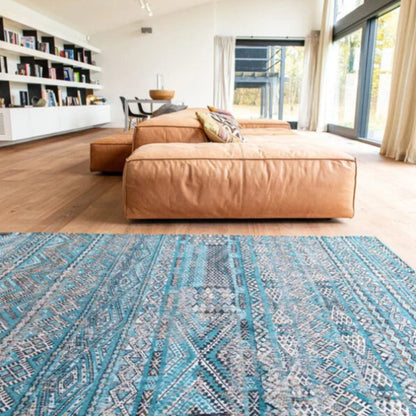 Blue patterned Louis De Poortere kilim rug in a modern living room with tan leather sofa and large windows