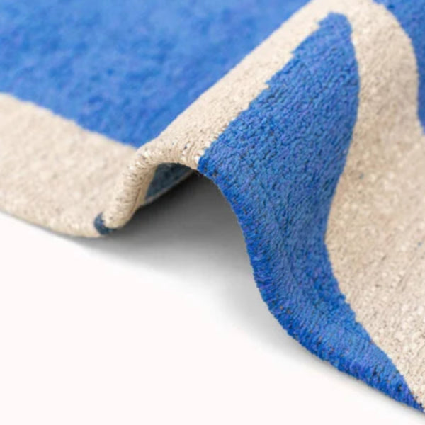 Close-up of folded Louis De Poortere Papercut rug showing blue and beige textured luxury fabric