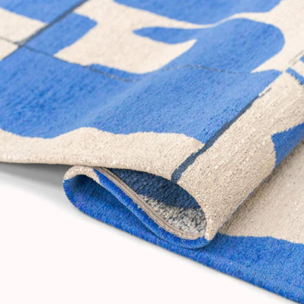 Close-up of folded Louis De Poortere Papercut rug showing blue and beige luxury woven texture