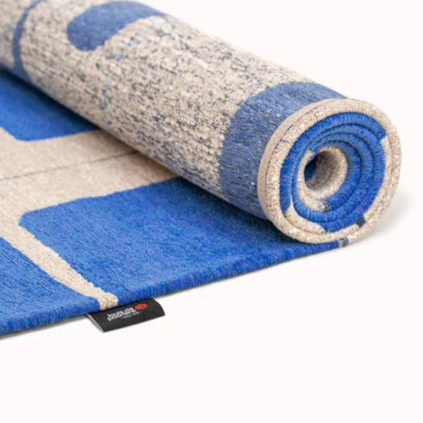 Rolled Louis De Poortere Papercut rug featuring blue and beige geometric patterns on luxury fabric
