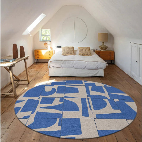 Round blue and beige Louis De Poortere Papercut rug on wooden floor in a bright bedroom with white walls and bed