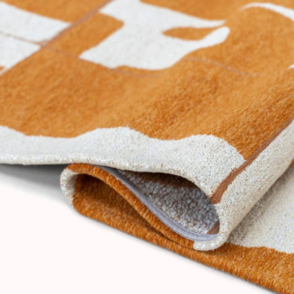 Close-up of folded Louis De Poortere Papercut rug in warm orange and beige tones with intricate design