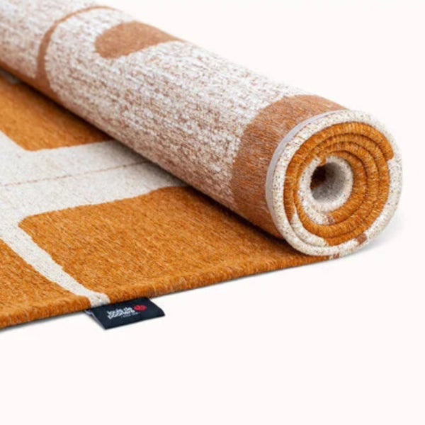 Rolled Louis De Poortere Papercut rug in warm orange and white tones with geometric patterns
