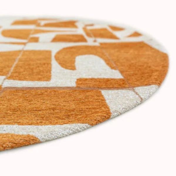 Close-up of round luxury Louis De Poortere Papercut rug in orange and white geometric design
