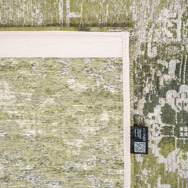 Close-up of green patterned Louis De Poortere Tabriz rug corner with woven texture and label