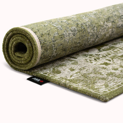 Rolled green Louis De Poortere Tabriz rug with intricate traditional pattern and soft texture