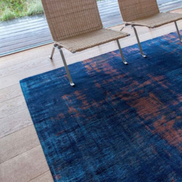 Louis De Poortere Venetian Dust rug in blue and copper hues under woven chairs on wooden flooring