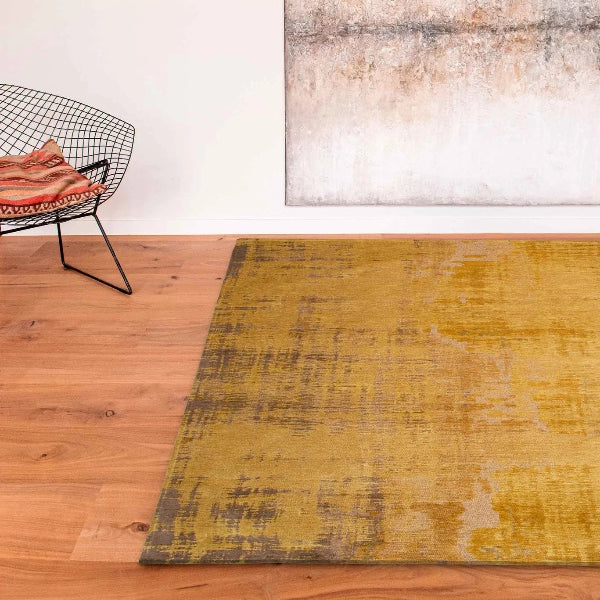 Louis De Poortere Venetian Dust rug in mustard yellow and brown tones on wooden floor with modern wire chair
