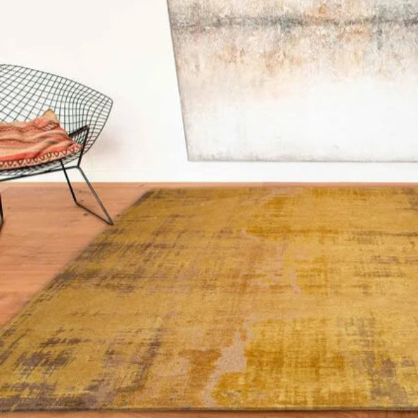 Louis De Poortere Venetian Dust rug in warm mustard tones on wooden floor with modern chair and abstract wall art