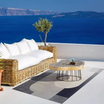 Outdoor patio with wicker sofa, table, and plants overlooking the ocean.