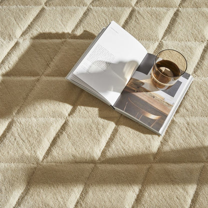 The Priory Wool Collection luxury rug in soft beige, styled with a book and glass of water